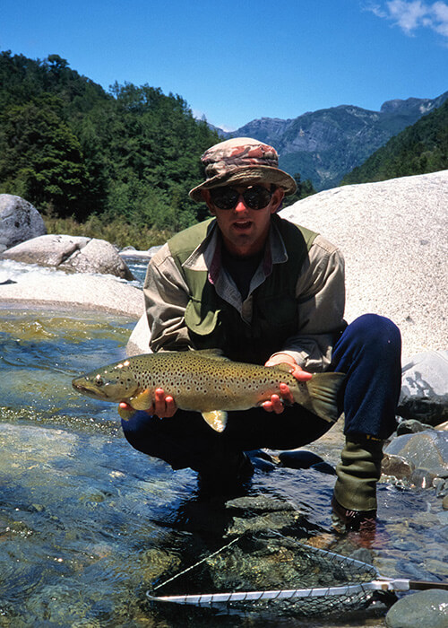 Man holding up a fresh caught trout with net below him.